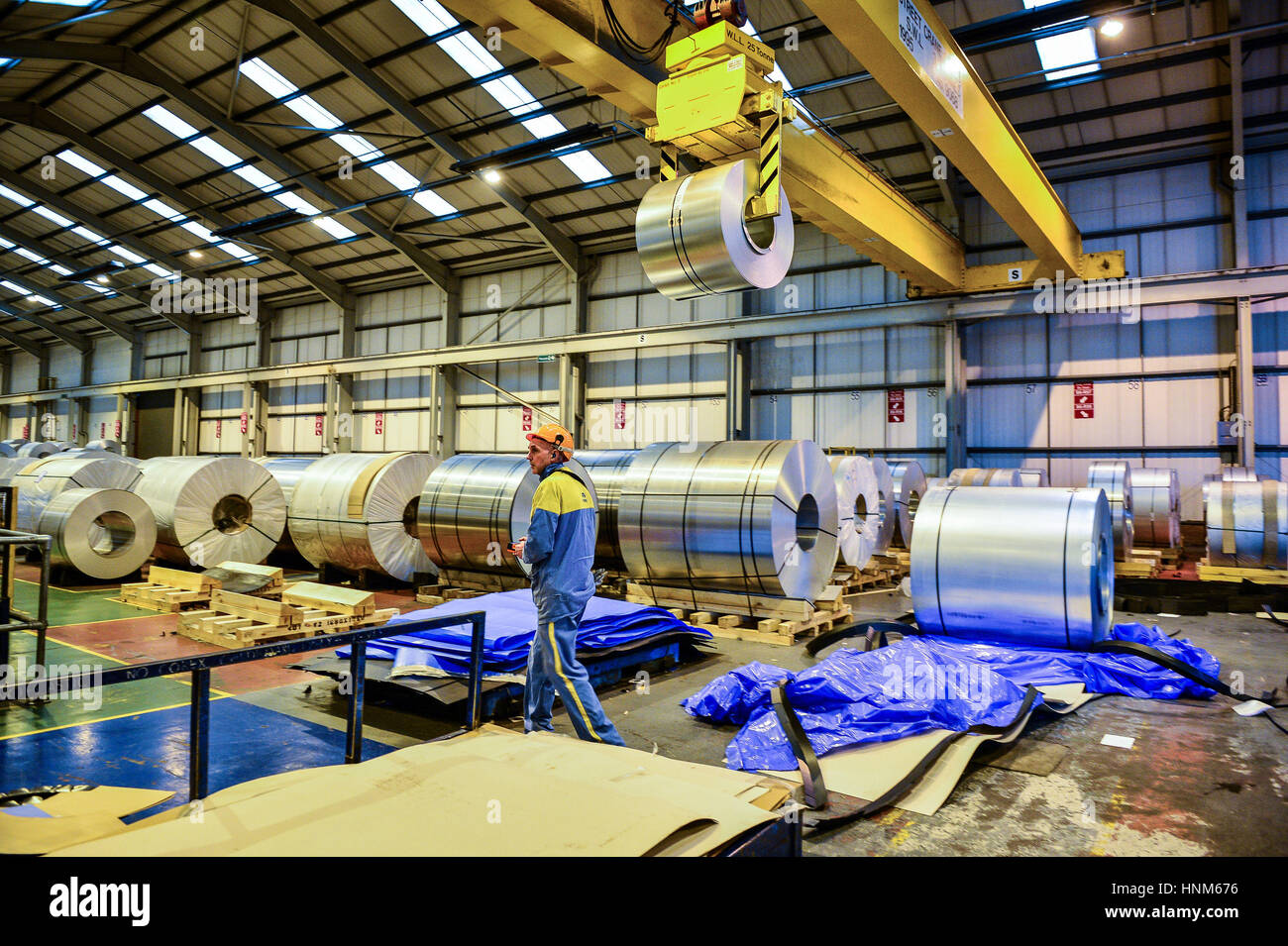 Ein Stahlarbeiter geht vorbei Rollen aus Stahl, die durch eine High-Tech-Roboter-Schweißanlage verwendet wird, wie es im Kfz-Service-Center am Tata Steel Wednesbury Standort Willenhall, Wolverhampton enthüllt wird. Stockfoto