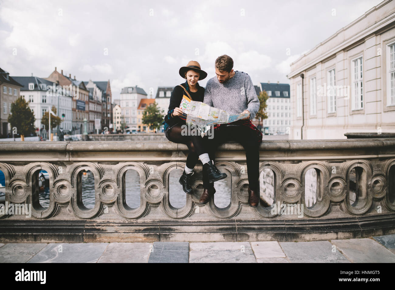 Junges Paar eine Navigationskarte sitzt auf einer Flussbrücke betrachten. Touristen, die Ausflüge in die Umgebung an bewölkten Tag. Stockfoto
