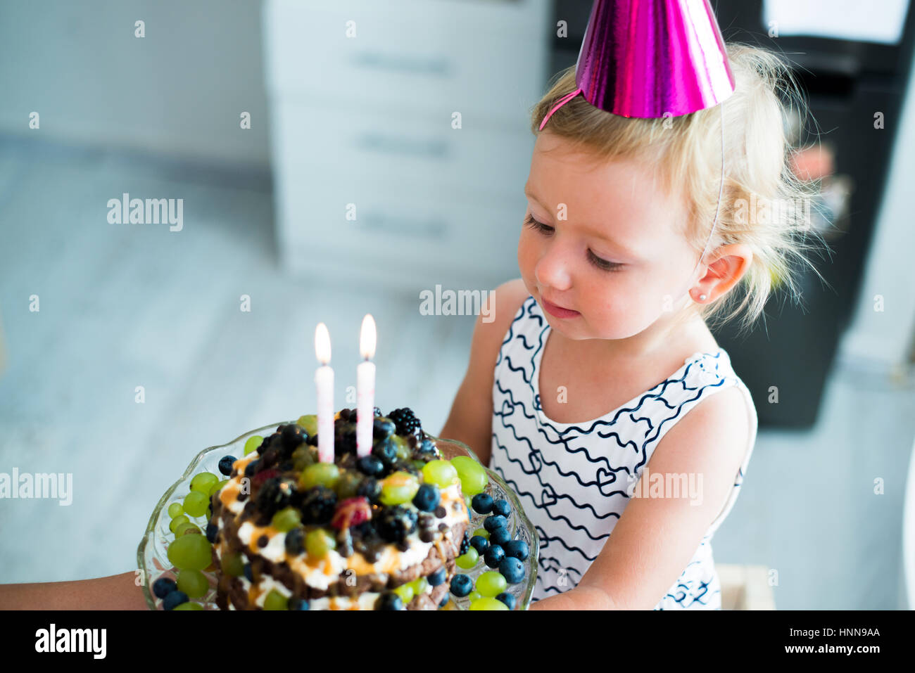 Niedliche kleine Mädchen mit ihrem Obst-Torte mit zwei Kerzen Stockfoto