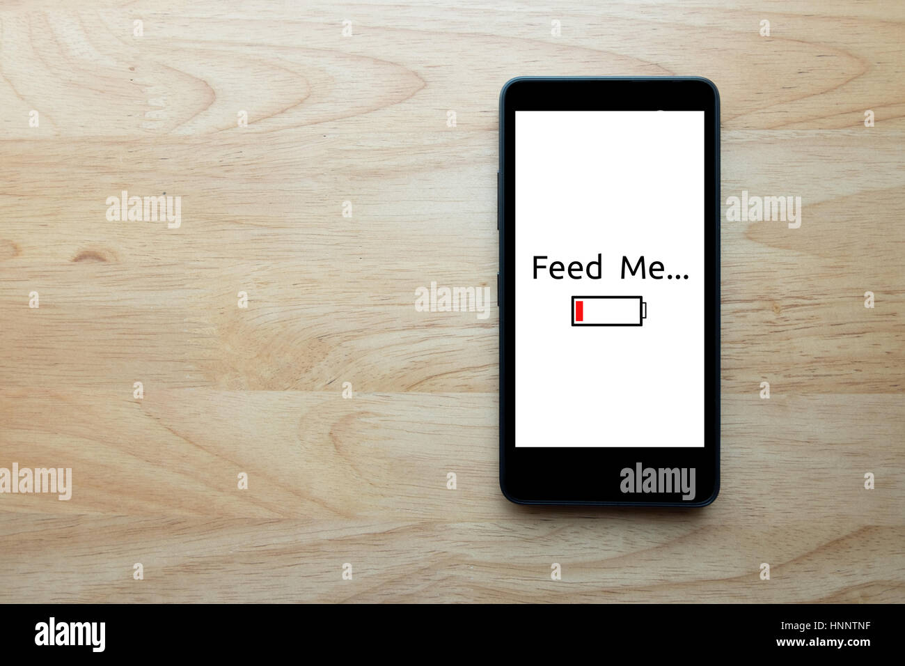 Smartphone Show Text auf Bildschirm "feed me" Status zeigen schwache Batterie mit Notebook auf Holztisch Hintergrund. Stockfoto