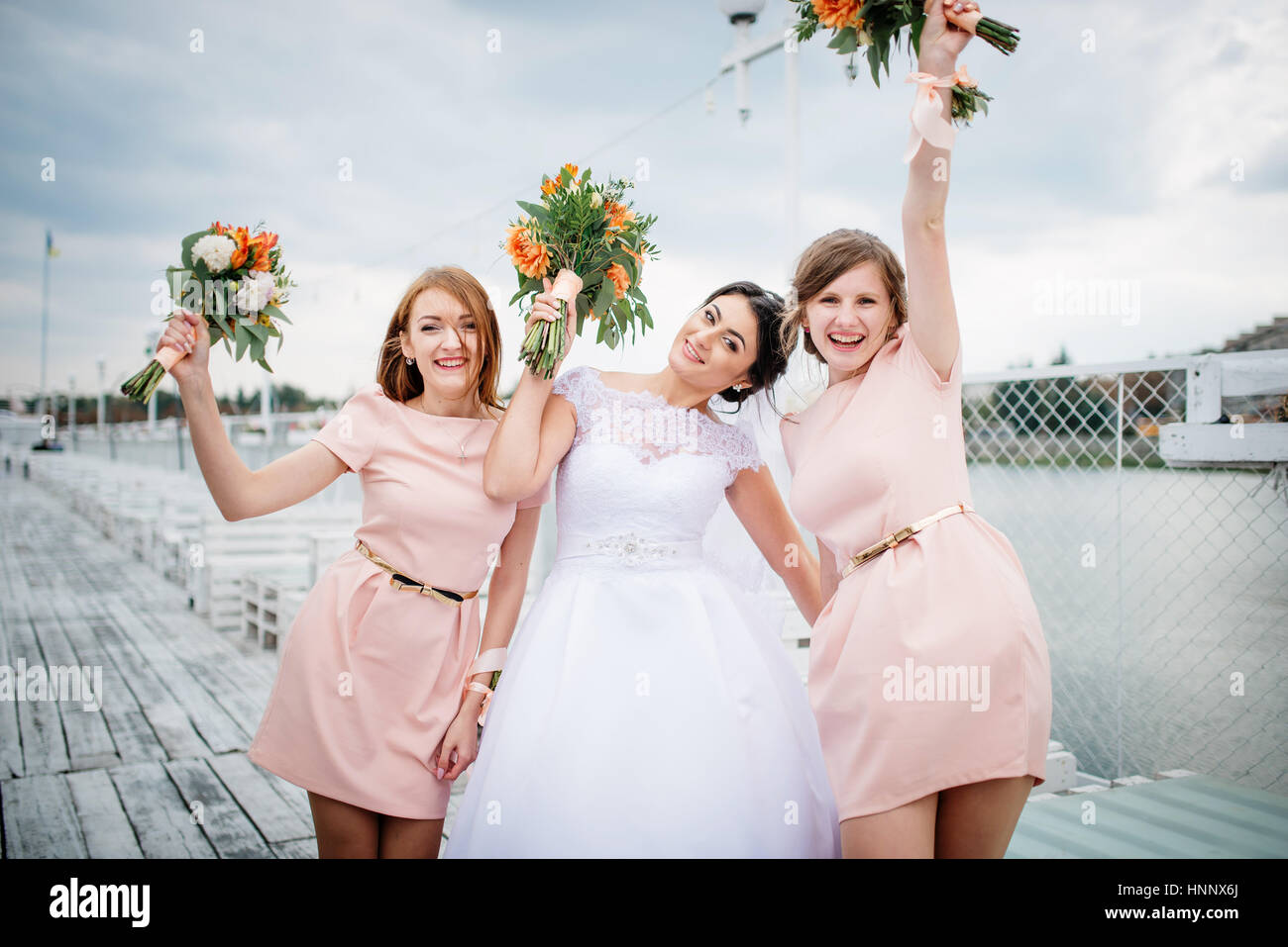 Braut mit Brautjungfern stellte auf der Pier-Liegeplatz am bewölkten Hochzeitstag. Stockfoto