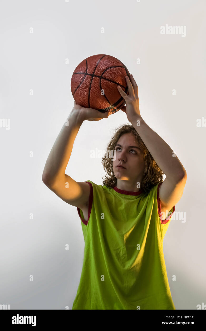 Junge mit blonden Haaren und ein grünes Trikot auf Basketball mit Schwerpunkt auf wirft den Ball zu spielen. Stockfoto