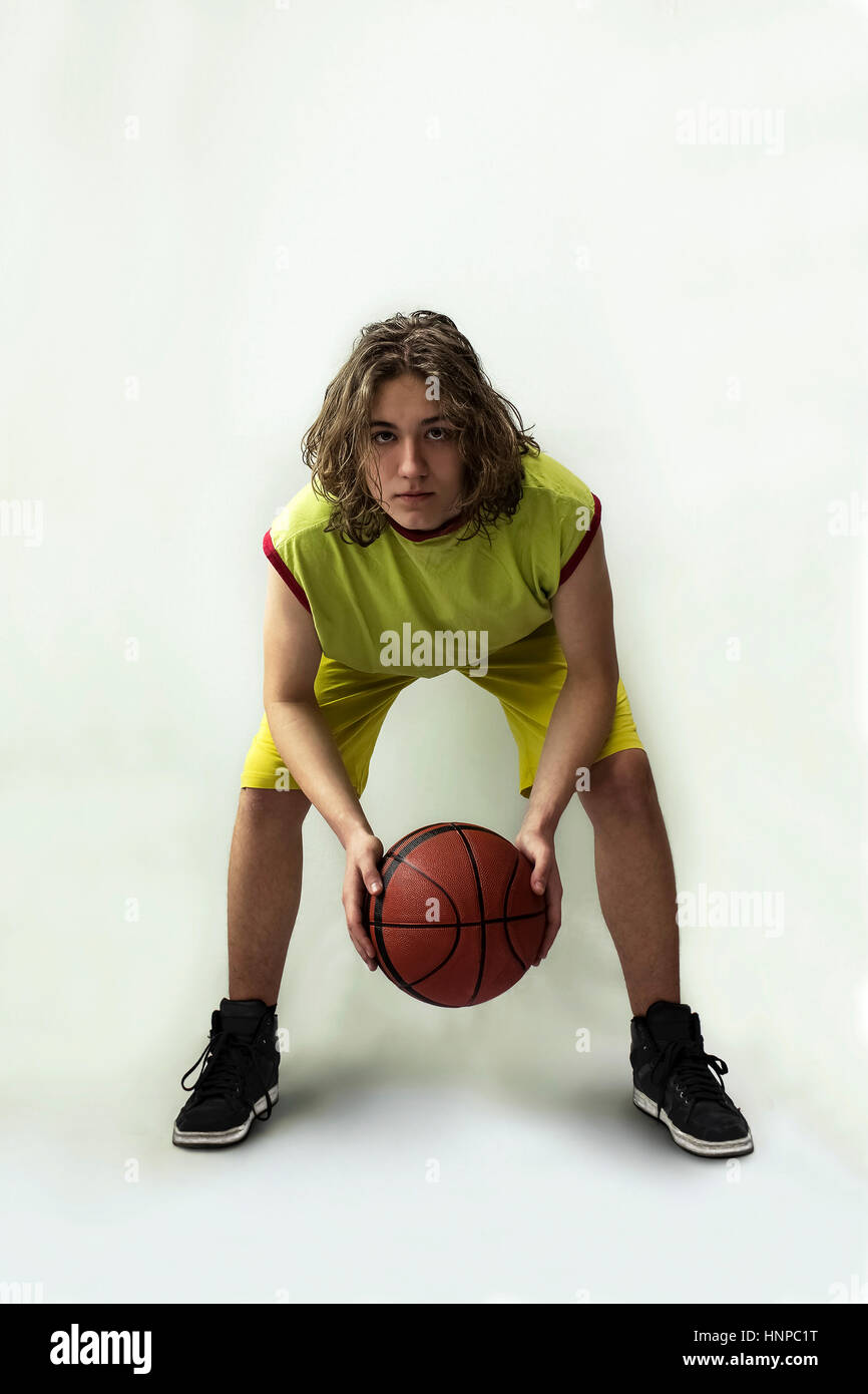 Kleiner Junge mit langen blonden Haaren, die mit einem grünen Trikot in einer hockenden Position halten einen basketball Stockfoto