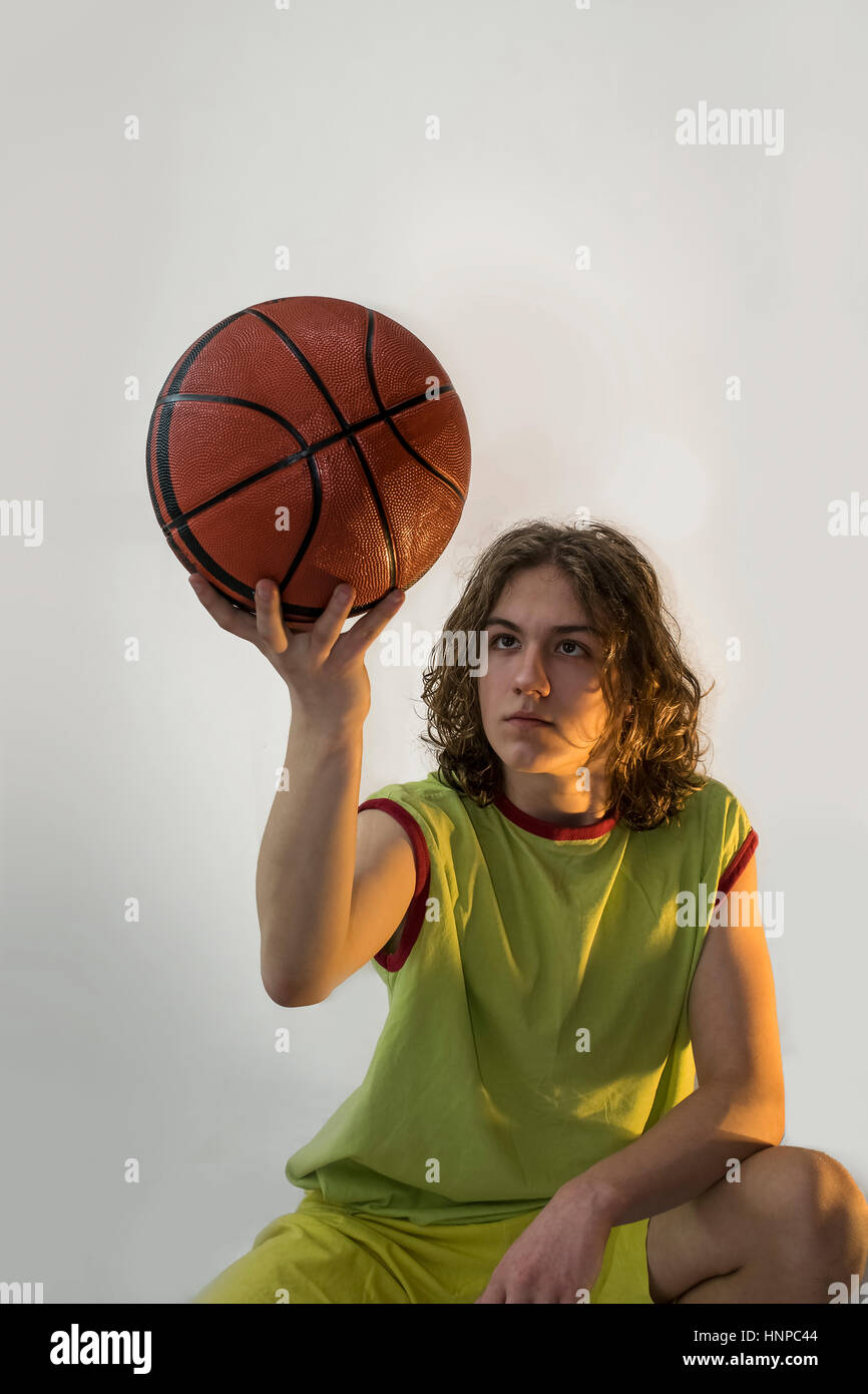 Junge mit langen blonden Haaren hochhalten und mit Blick auf einen Basketball beim hinsetzen. Stockfoto