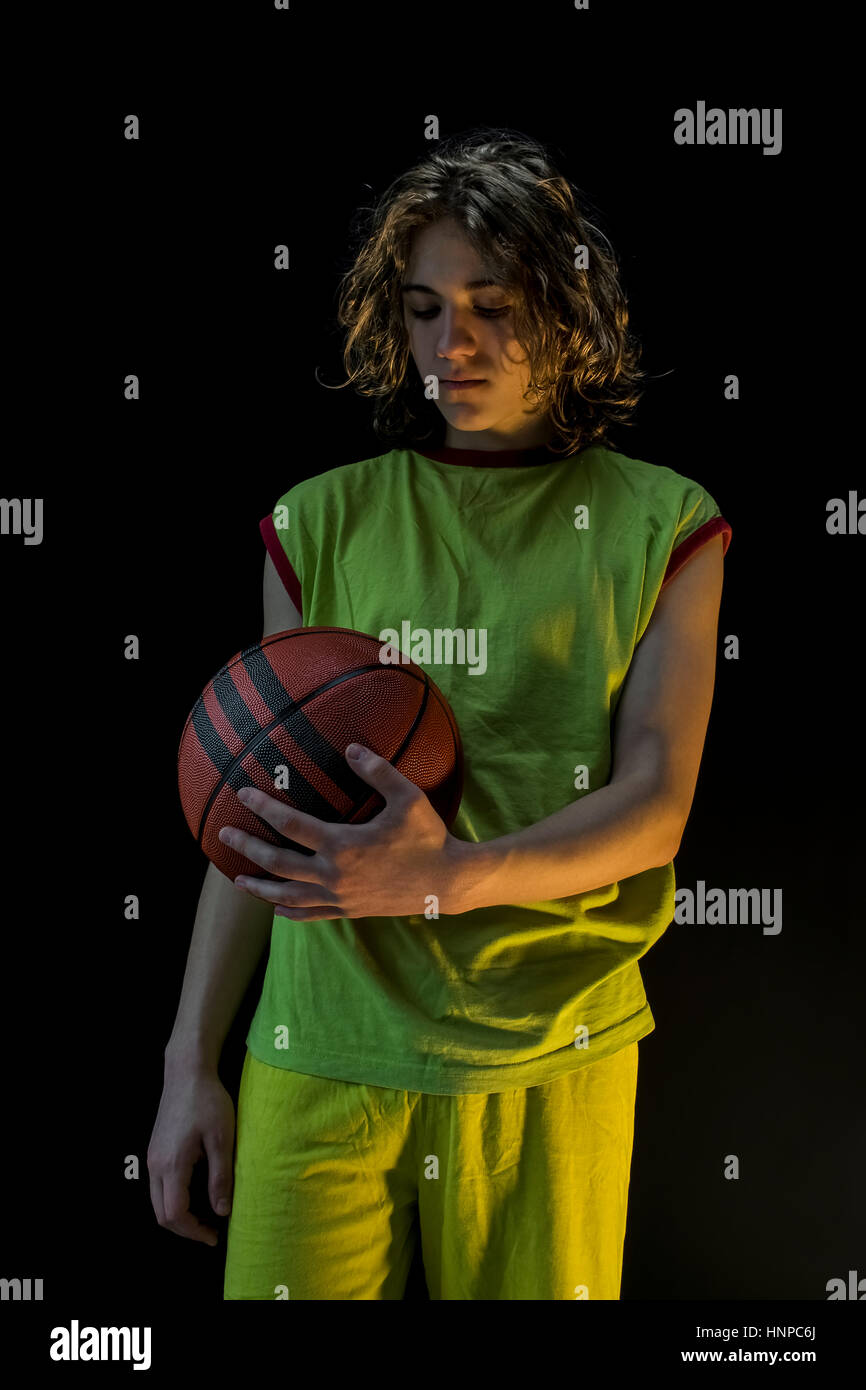 Junge mit langen blonden Haaren, die mit einem grünen Trikot halten und blickte auf einen Basketball. Stockfoto