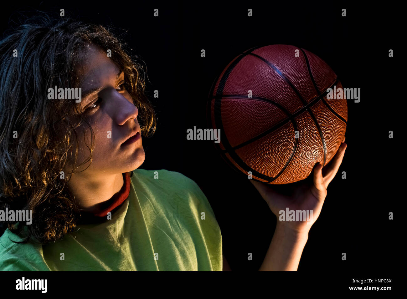 Nahaufnahme eines kleinen Jungen mit langen blonden Haaren, die mit einem grünen Trikot hält einen Basketball. Stockfoto