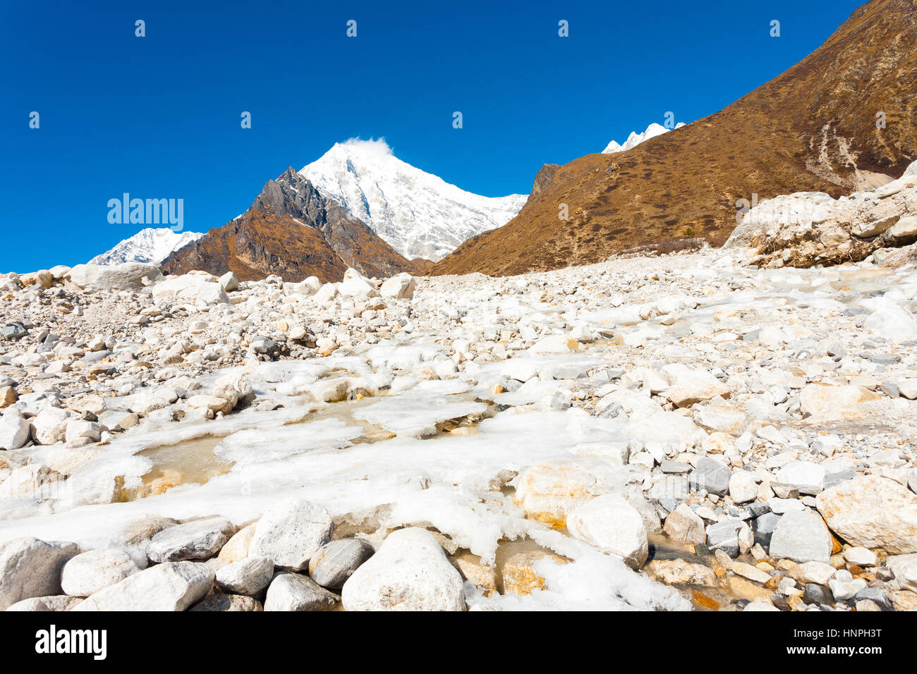 Eisigen alpinen Fluss, der durch weiße felsiges Gelände Landschaft in Höhenlage alpine Tundra mit Langtang Lirung Peak Hintergrund in der Nähe von Kyanjin Gompa Stockfoto