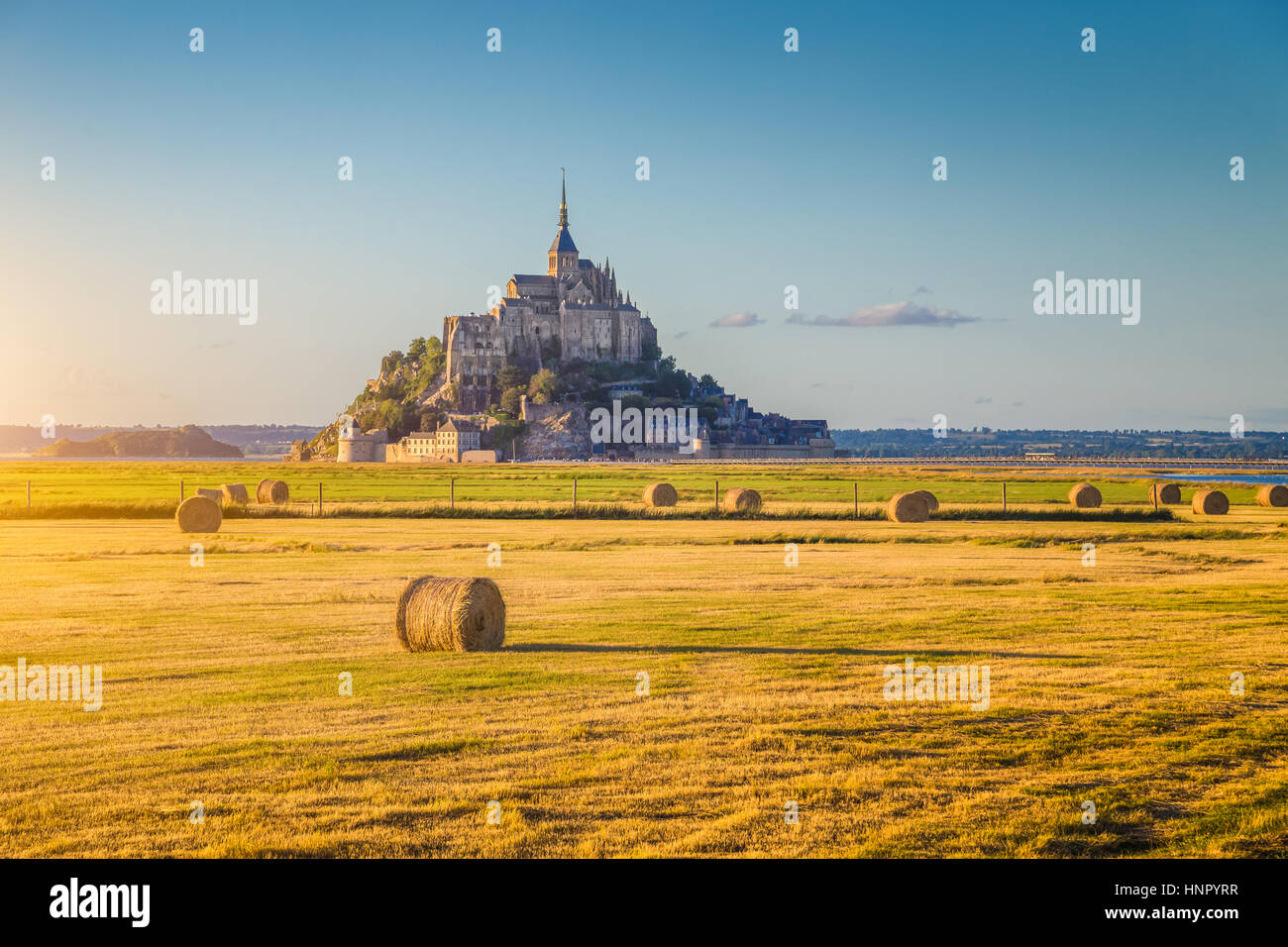 Schöne Aussicht von berühmten historischen Le Mont Saint-Michel im goldenen Abendlicht bei Sonnenuntergang im Sommer mit Heuballen auf Feldern, Normandie, Nordfrankreich Stockfoto