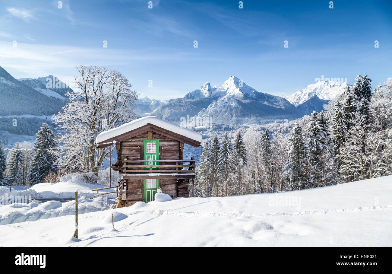 Panoramablick auf malerische weiße Winter Wunderland Bergkulisse der Alpen mit traditionellen hölzernen Almhütte an einem kalten, sonnigen Tag mit blauem Himmel Stockfoto