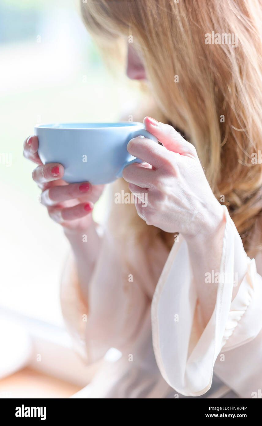 Eine Frau hält eine Tasse Kaffee in einem blauen Becher. Stockfoto