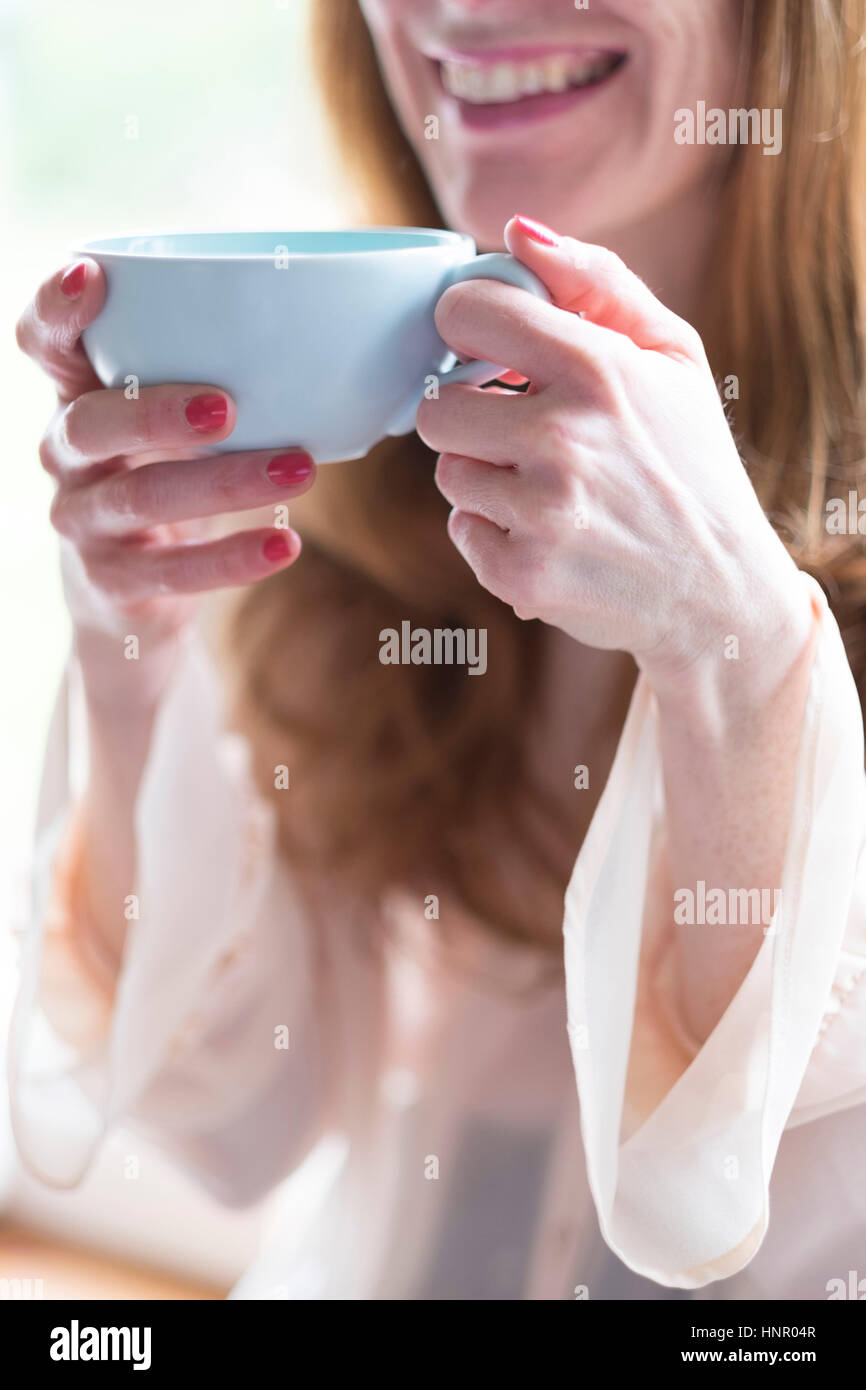 Eine Frau hält eine Tasse Kaffee in einem blauen Becher. Stockfoto