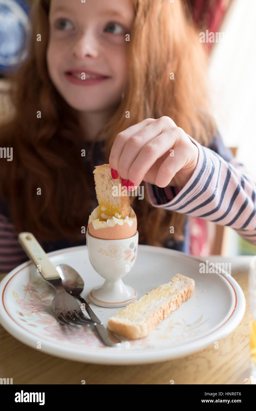 Ein kleines Mädchen essen ein Ei aus einem Ei-Cup beim Frühstück Stockfoto