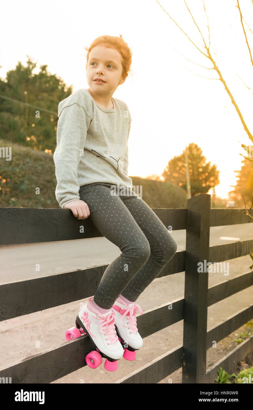 Ein kleines Mädchen sitzt auf einem Zaun in Rollschuhe Stockfoto