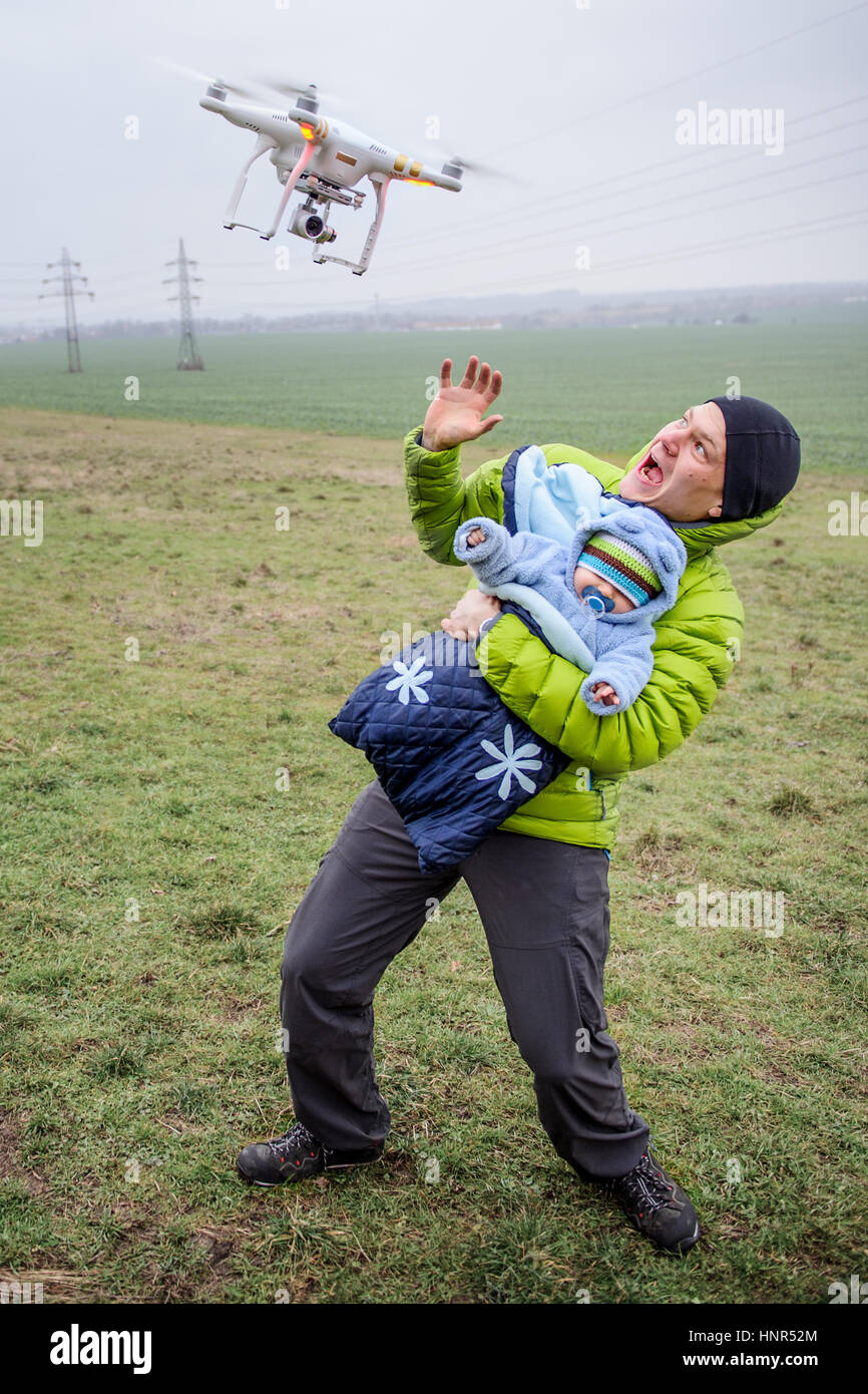 Man schützt seine Baby gegen eine angreifende Drohne. Gefährliche Drohne Closeup zu verängstigt Elternteil mit Kind in armen Stockfoto