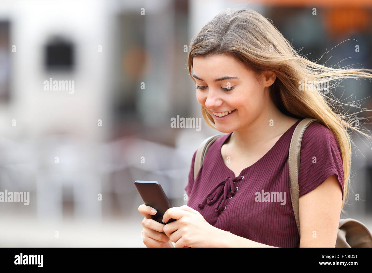 Glückliches Mädchen gehen und Schreiben von Nachrichten auf dem Handy auf der Straße Stockfoto