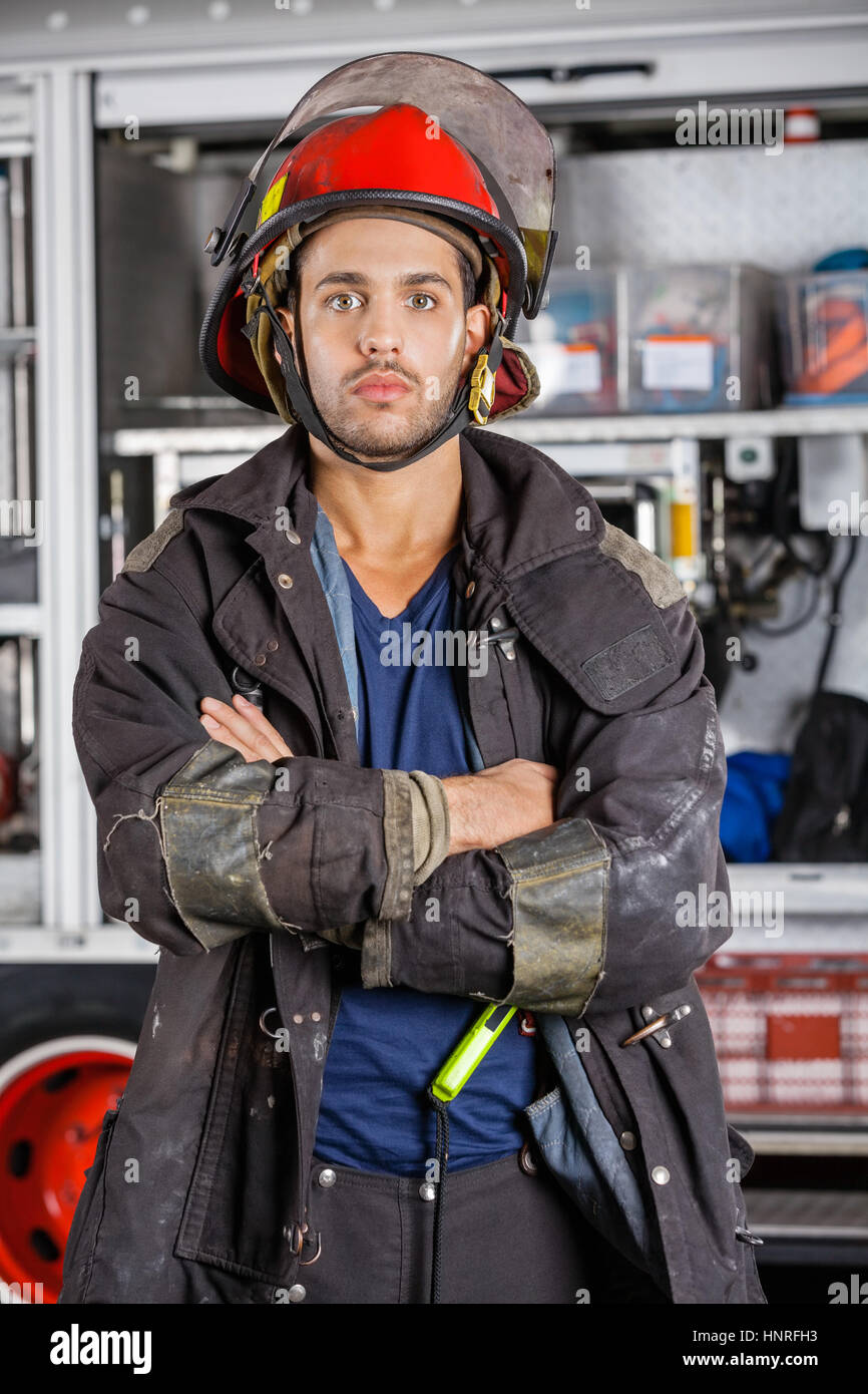 Ernsthafte Feuerwehrmann Stand mit verschränkten Armen gegen Feuerwehrauto Stockfoto