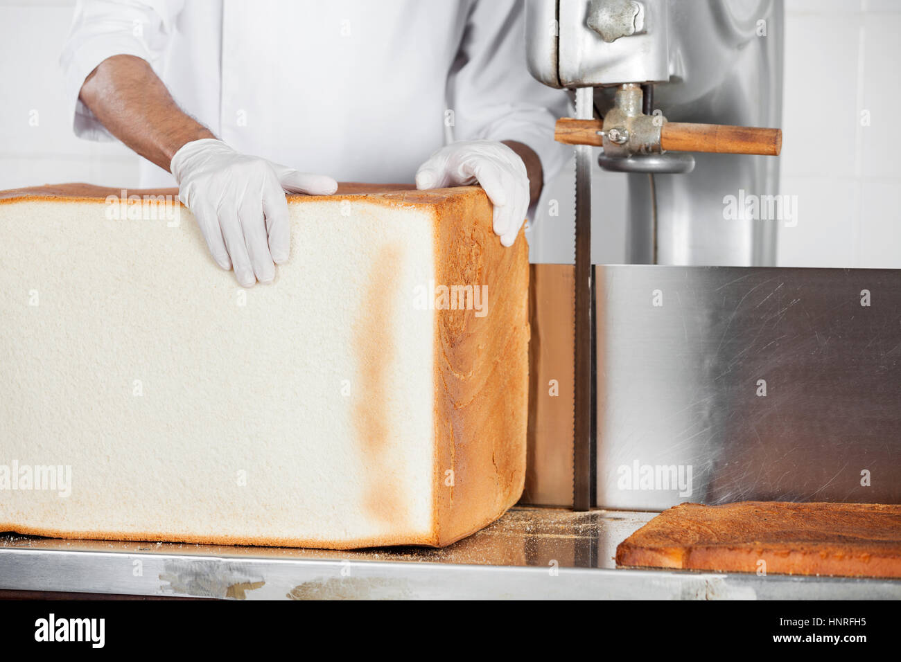 Baker Holding Großer Brotlaib an der Schneidemaschine in Bäckerei Stockfoto