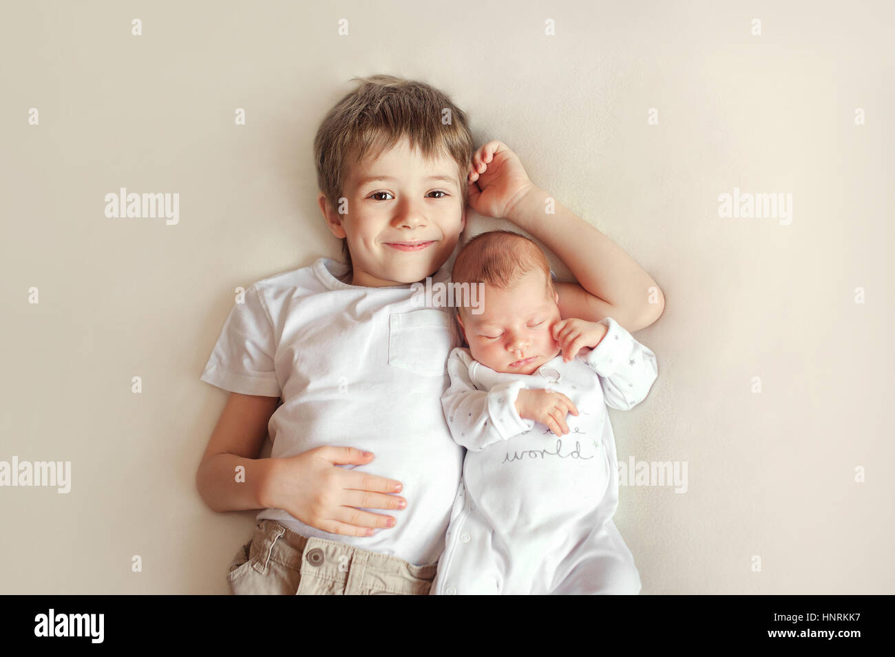 Kleiner Bruder umarmt ihr neugeborenes Baby. Kleinkind Kind treffen neues Geschwisterchen. Süsser Boy und Neugeborenen Mädchen entspannen Sie sich in eine weiße Schlafzimmer. Familie mit Kindern zu Hause. Liebe, Vertrauen und Zärtlichkeit Stockfoto