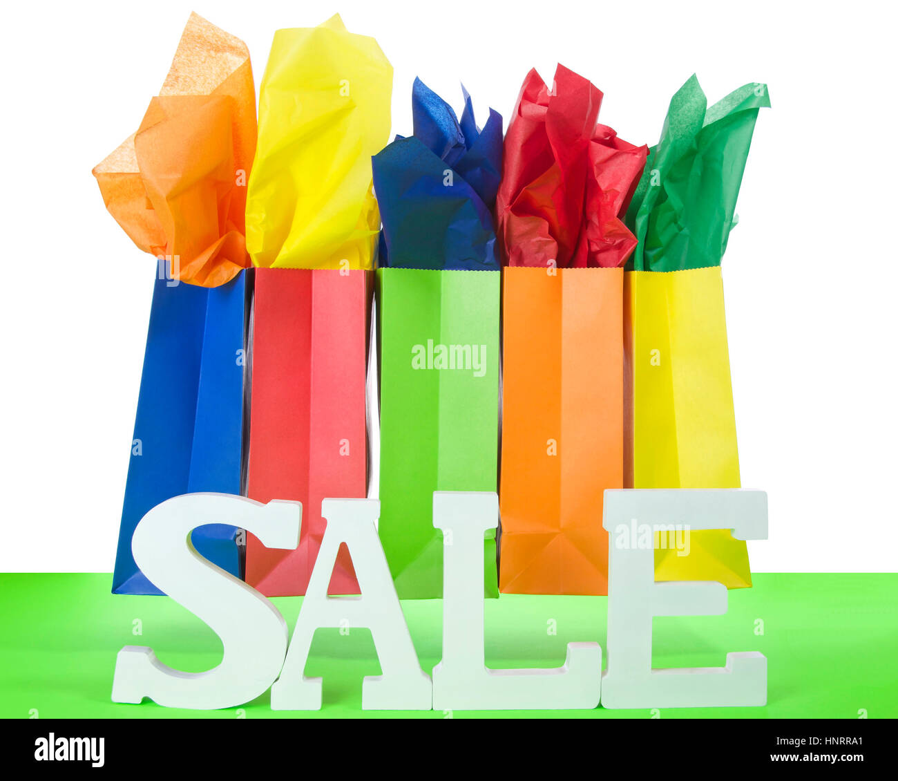 bunte Taschen mit hellem Seidenpapier fügt auf einem roten Tisch mit weißem Hintergrund und Verkauf Buchstaben. Holiday Sale Stockfoto