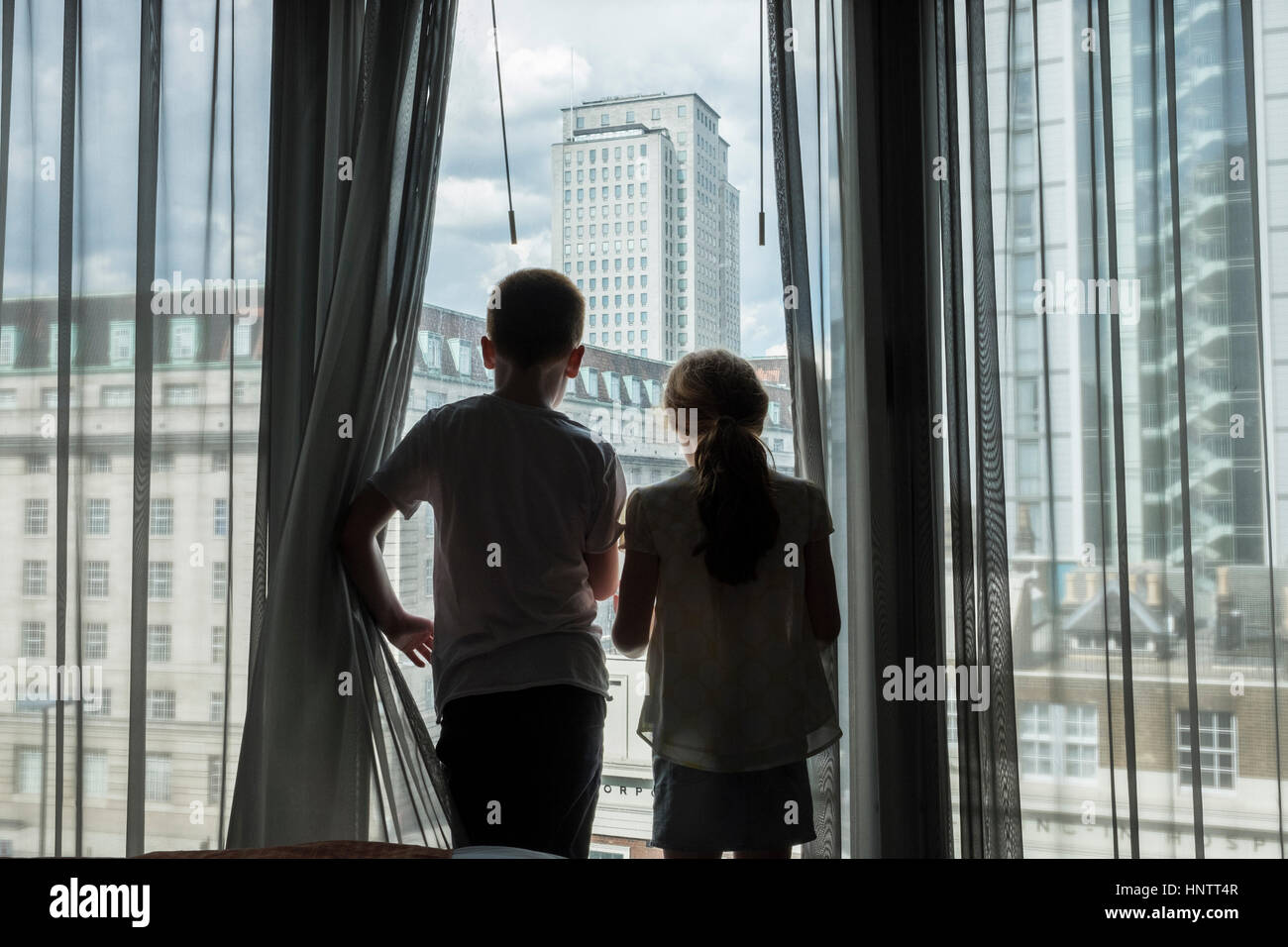 Ein Junge und Mädchen, die durch ein hohes Fenster in einer Stadt suchen. Stockfoto