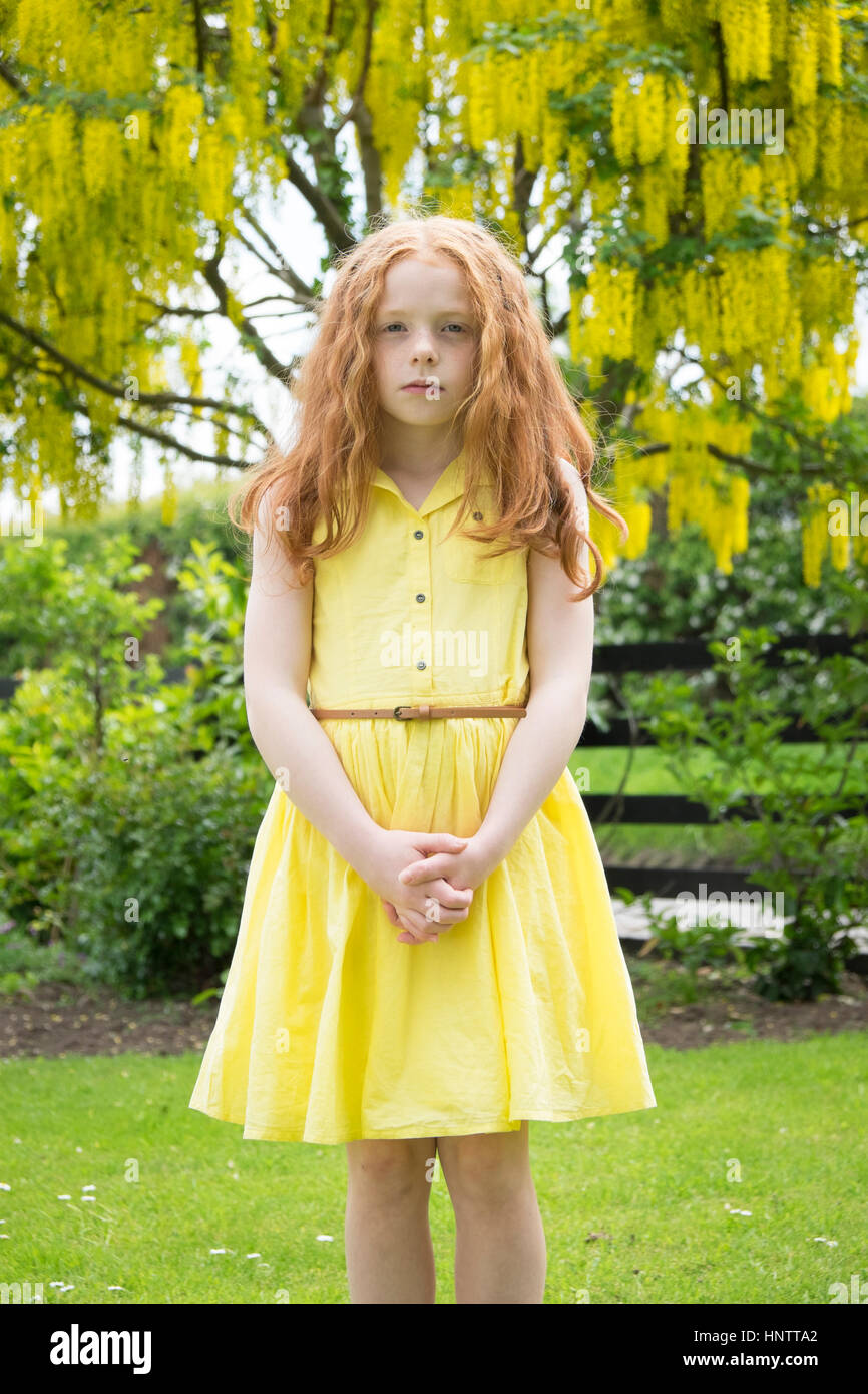 Ein kleines Mädchen im gelben Kleid stehen vor einem gelben Baum. Stockfoto