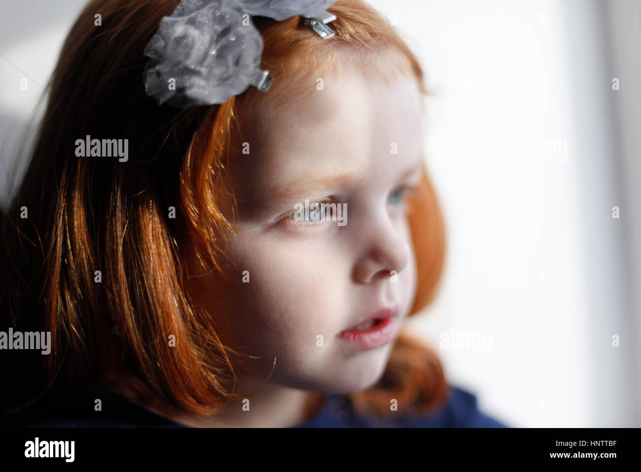 Ein 4 Jahre altes Mädchen mit Ingwer Haar sieht aus dem Fenster Stockfoto
