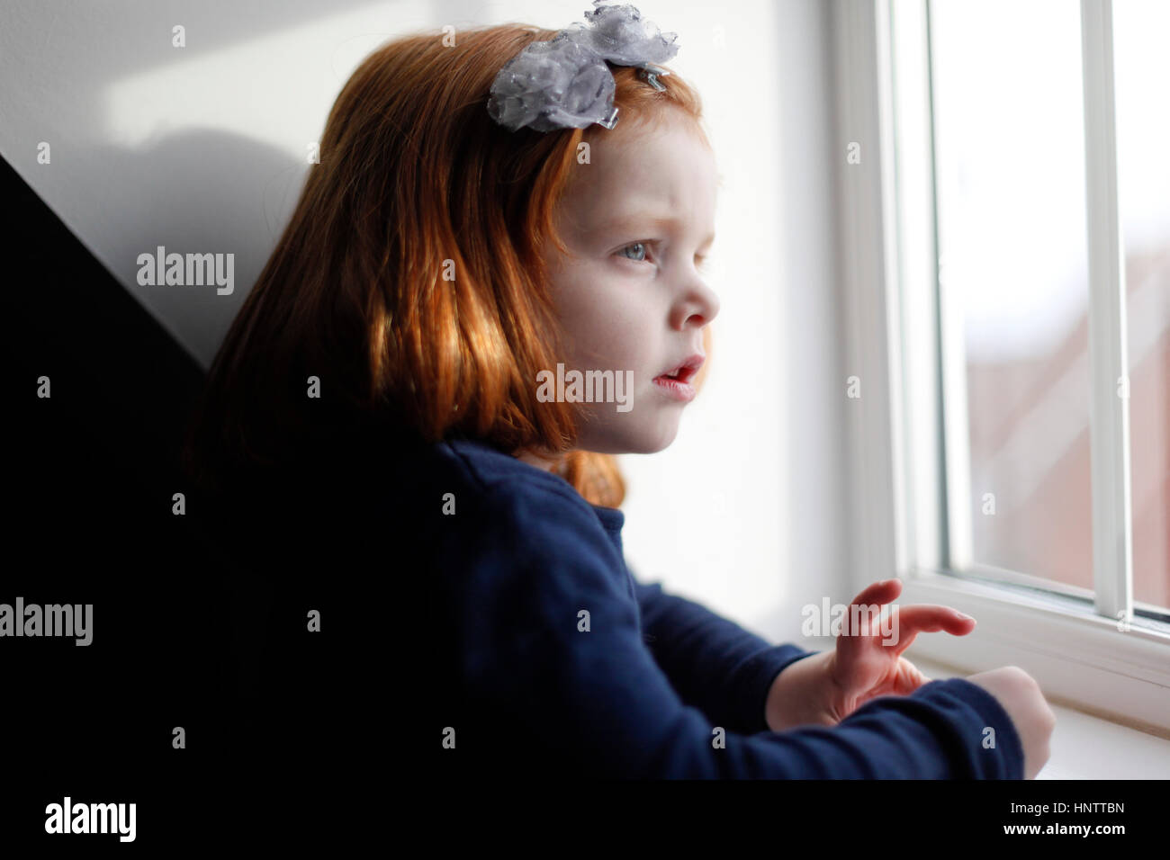 Ein 4 Jahre altes Mädchen mit Ingwer Haar sieht aus dem Fenster Stockfoto