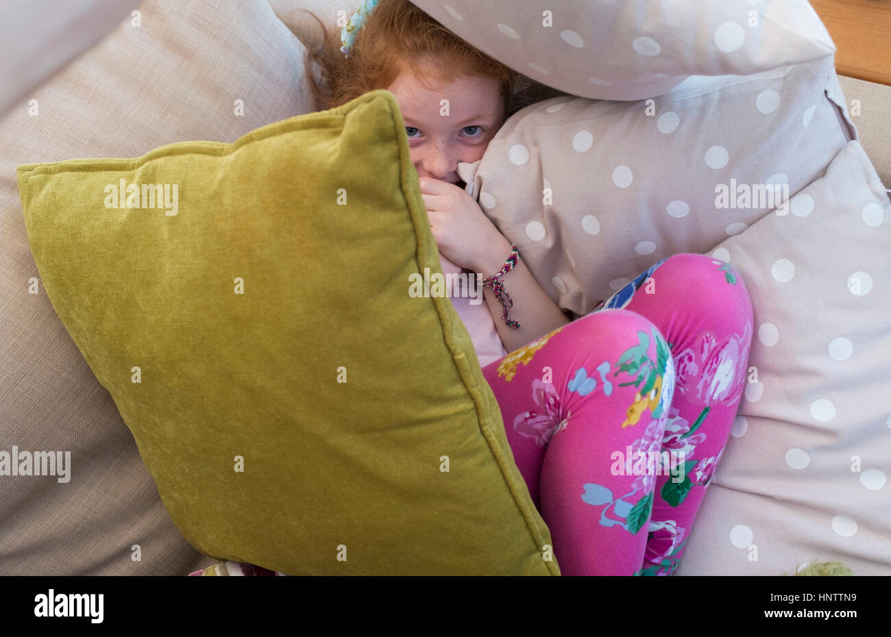 Ein kleines Mädchen versteckt sich unter einigen Kissen Stockfoto