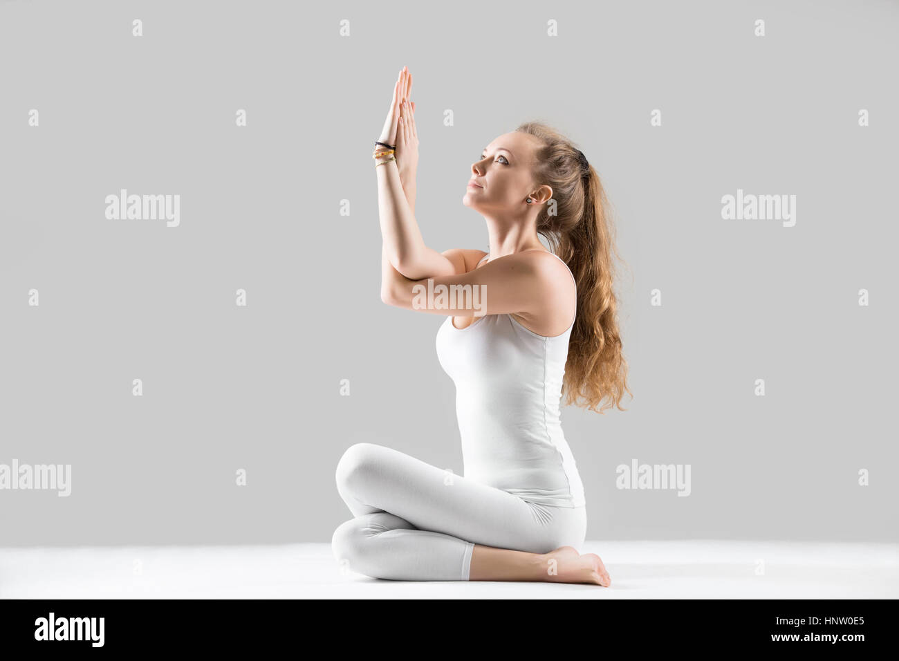 Junge Frau sitzt in Kuh-Gesicht-Pose, graue Studio-Hintergrund Stockfoto