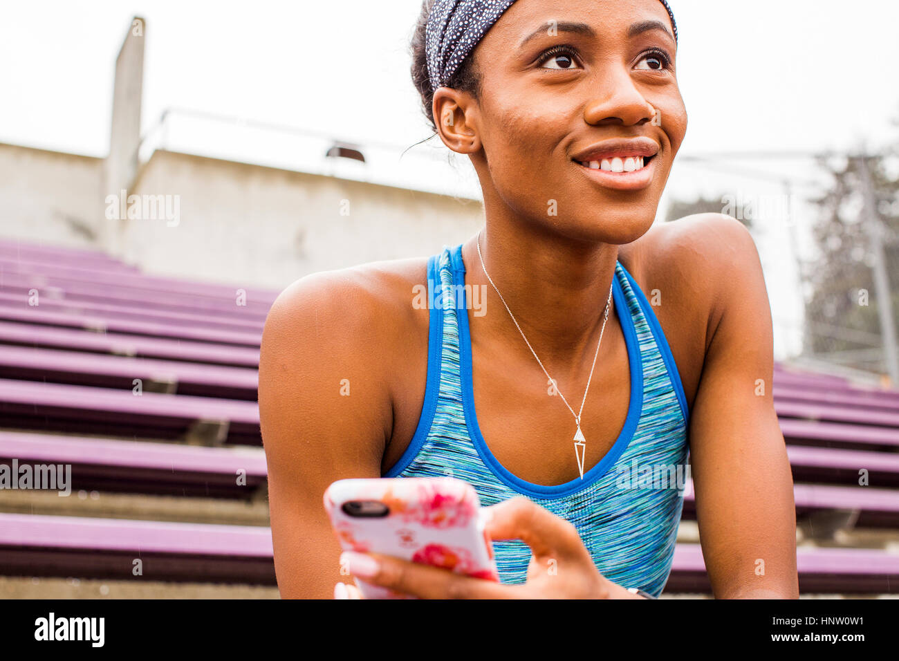 Lächelnde schwarze Frau sitzt auf der Tribüne SMS auf Handy Stockfoto