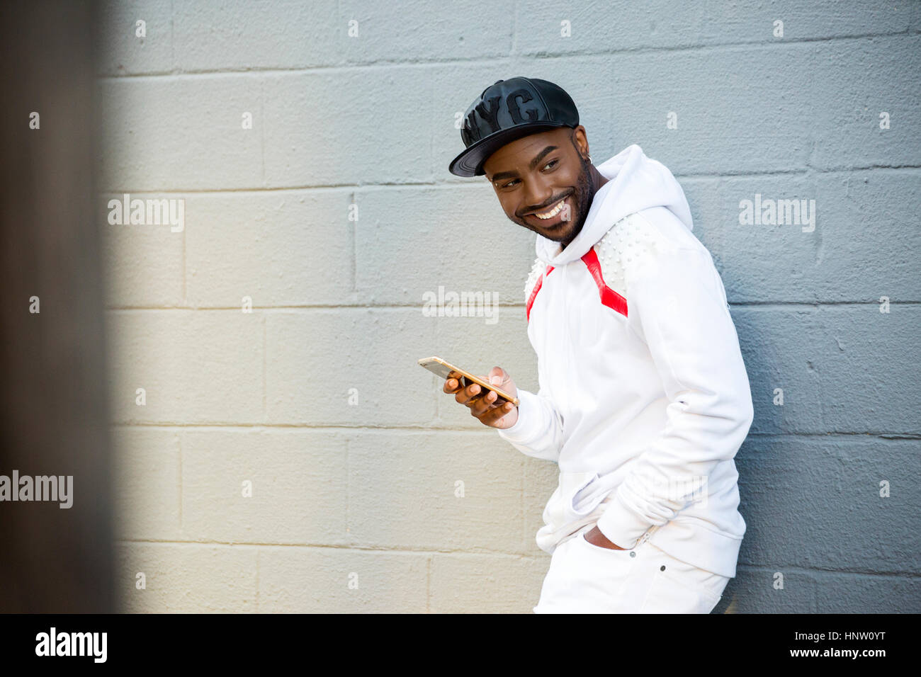 Lächelnder schwarzen Mann stützte sich auf Wand hält Handy Stockfoto