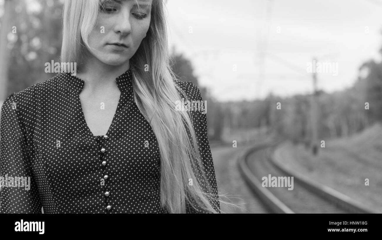 schwarz / weiss Portrait einer jungen blonden Frau mit langen Haaren in einem altmodischen Kleid, stehend mit einem traurigen nachdenklichen Ausdruck auf seinem Gesicht auf th Stockfoto