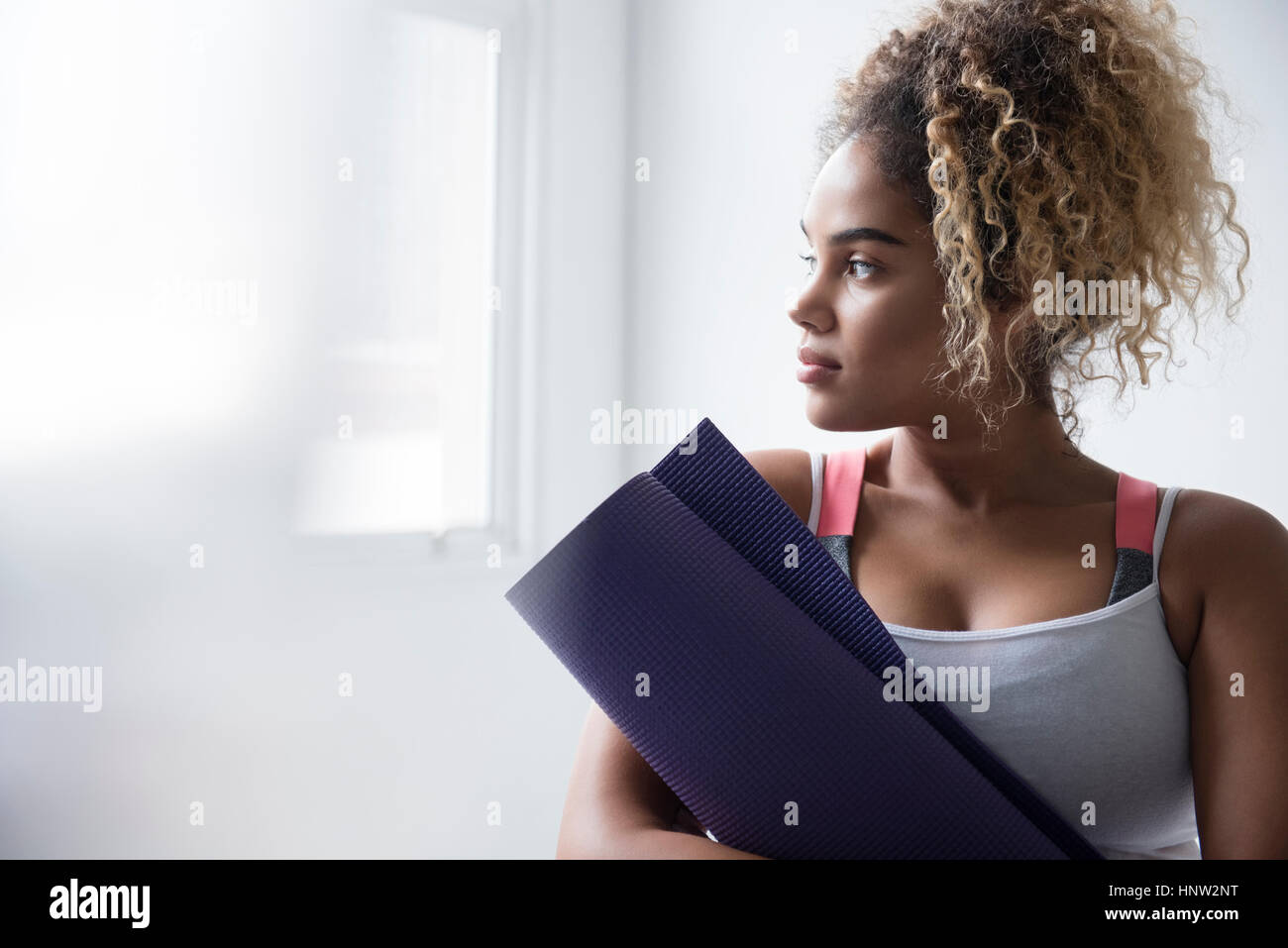 Nachdenklich Mischlinge Frau hält aufgerollt Gymnastikmatte Stockfoto