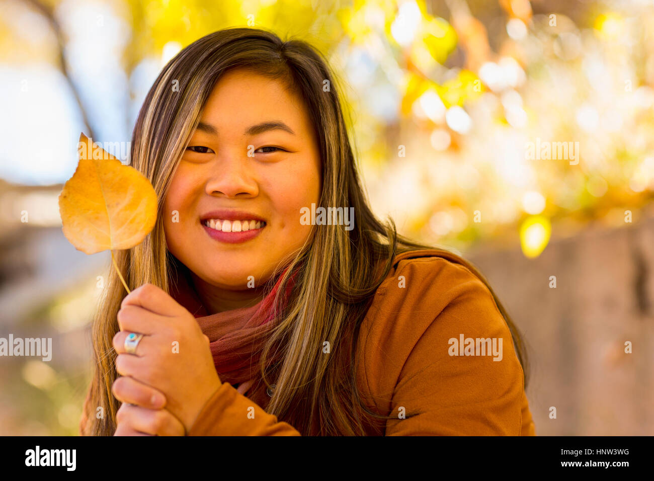 Lächelnde asiatische Frau hält Blatt im Herbst Stockfoto