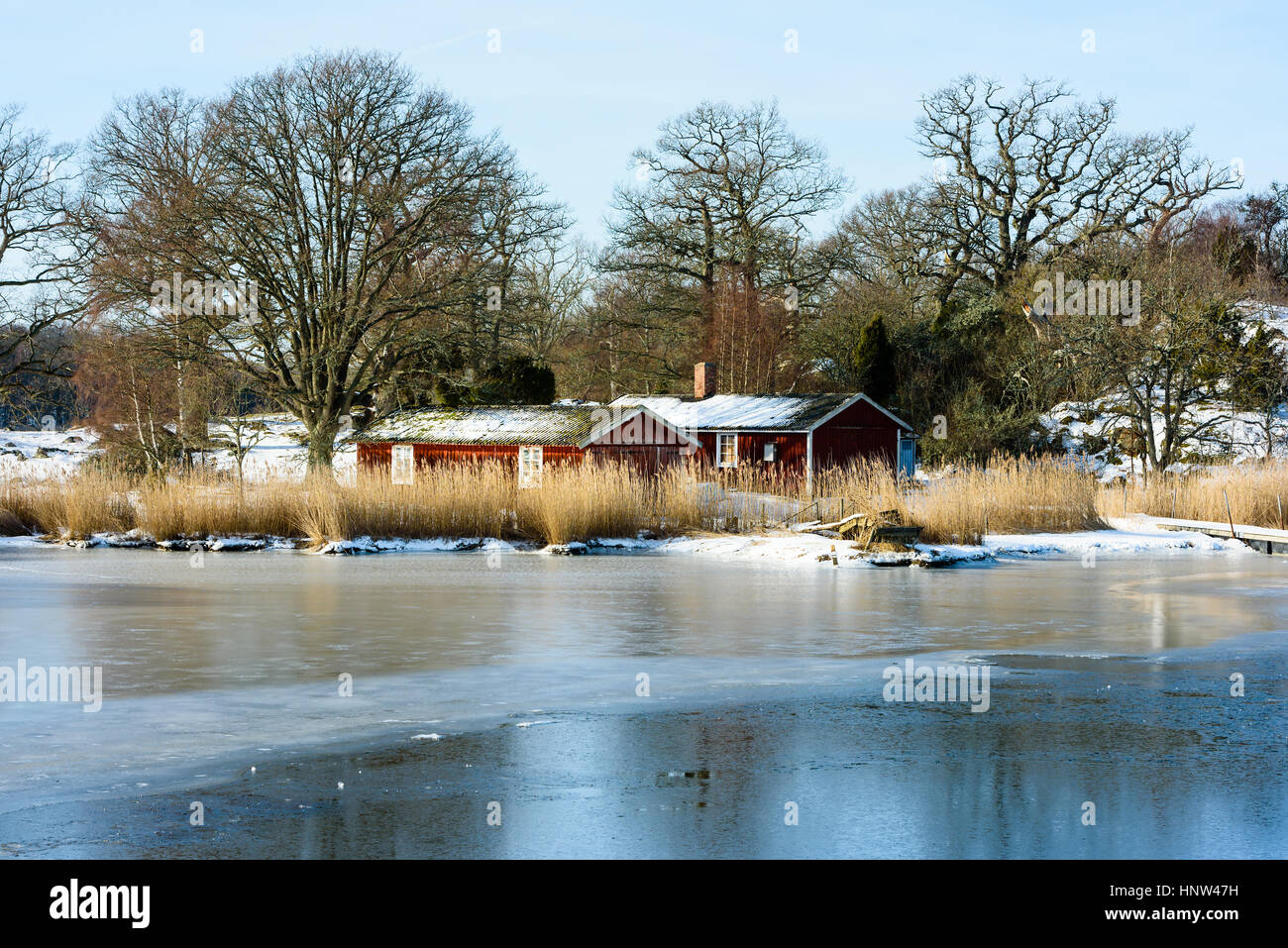 Zwei hölzerne Hausboote unter Reed in die Küste im Winter. Vereister Schnee auf Land und Meer. Küsten Wald hinter Gebäuden. Lage Hjortahammar in Stockfoto