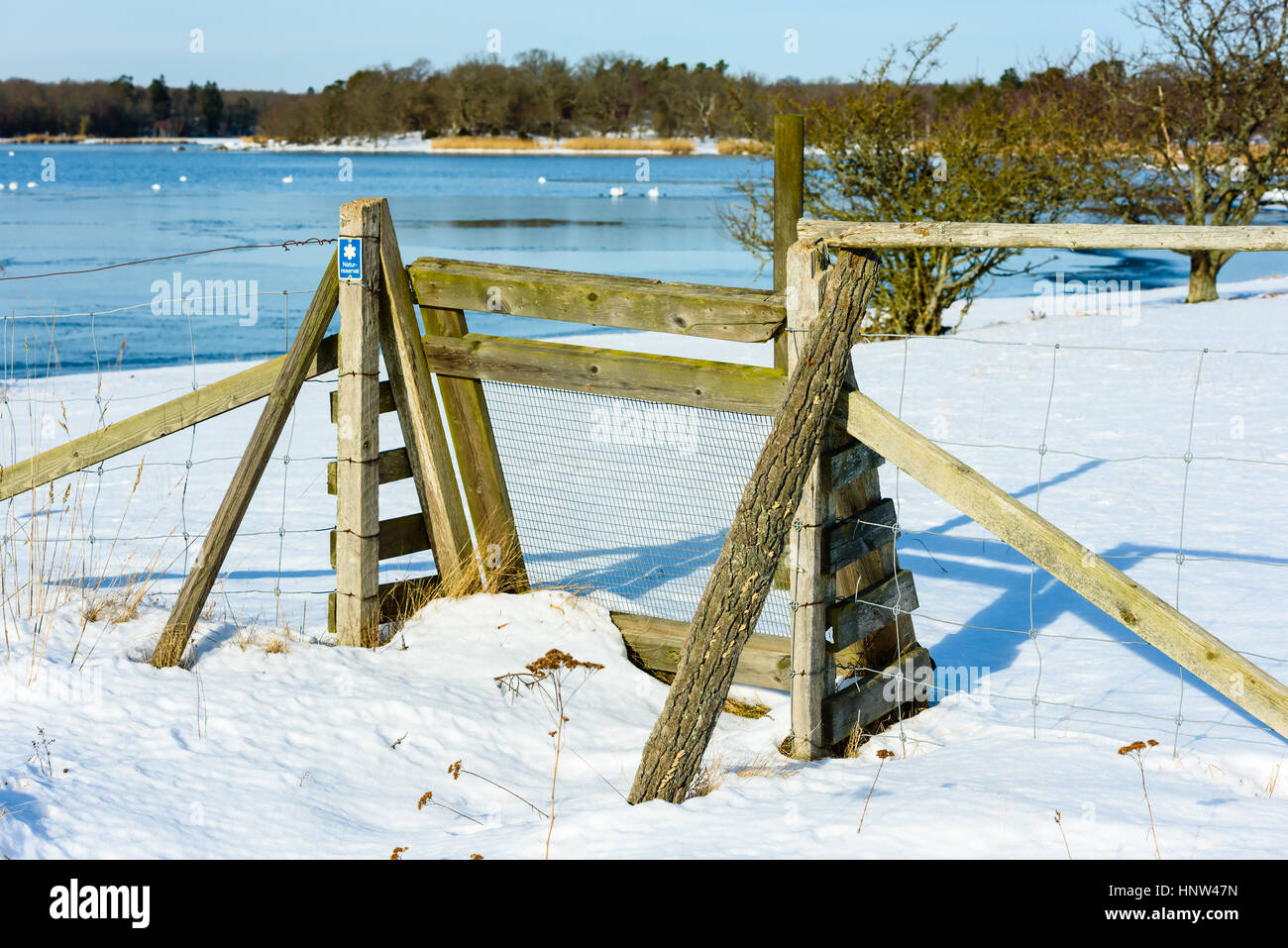 Kleines Tor zur Küste Natur reserve im Winter. Blaues Schild auf Post sagt Naturschutzgebiet in schwedischer Sprache. Landschaft mit Vögel im Wasser verschwommen im Hintergrund. Stockfoto