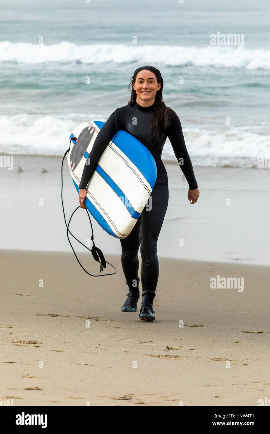Kaukasische Trägerin Neoprenanzug tragen Surfbrett am Strand Stockfoto