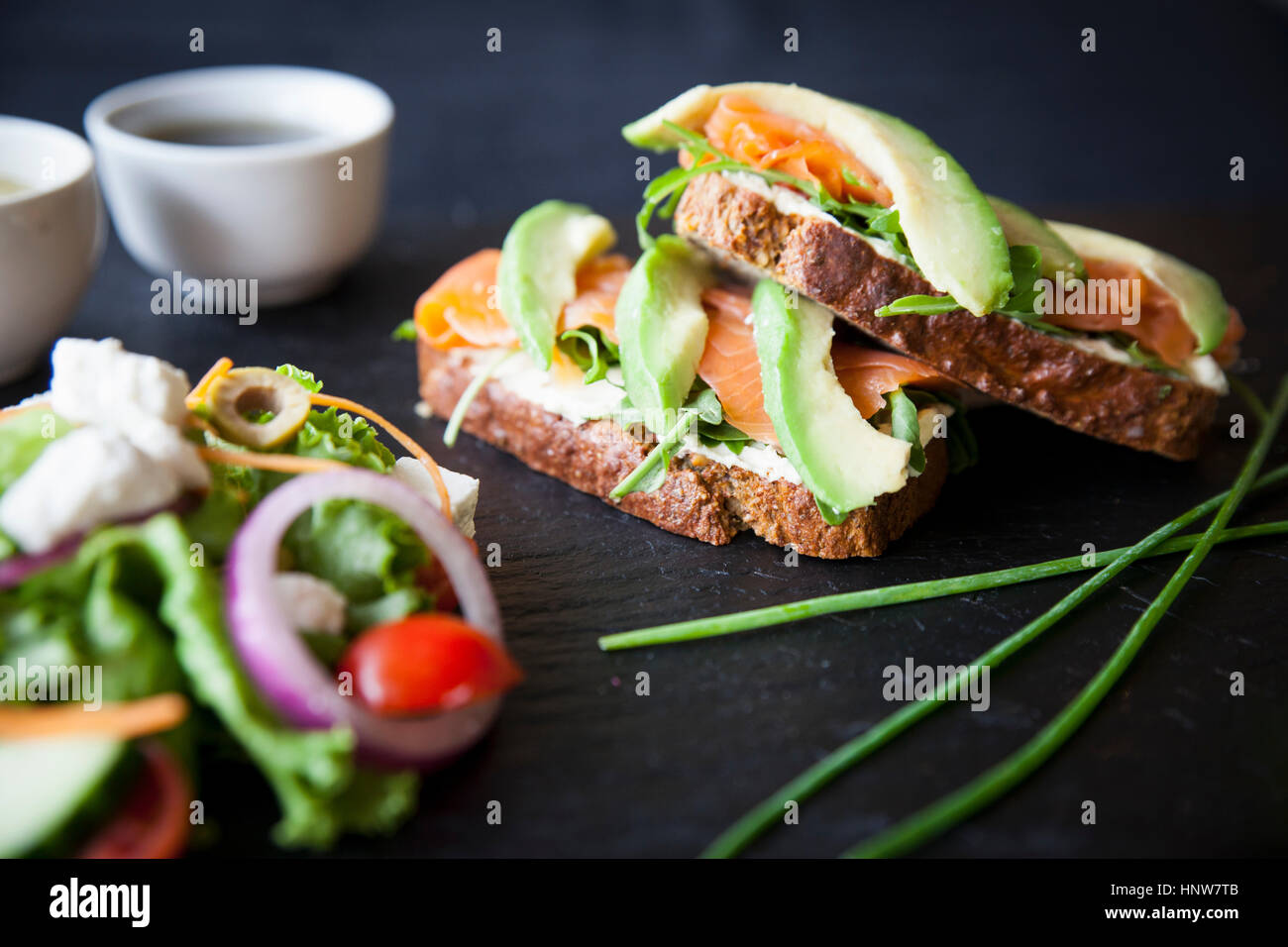 Geräucherter Fisch und Avocado belegte Brötchen mit Salat und Dip Saucen auf Schiefer Stockfoto