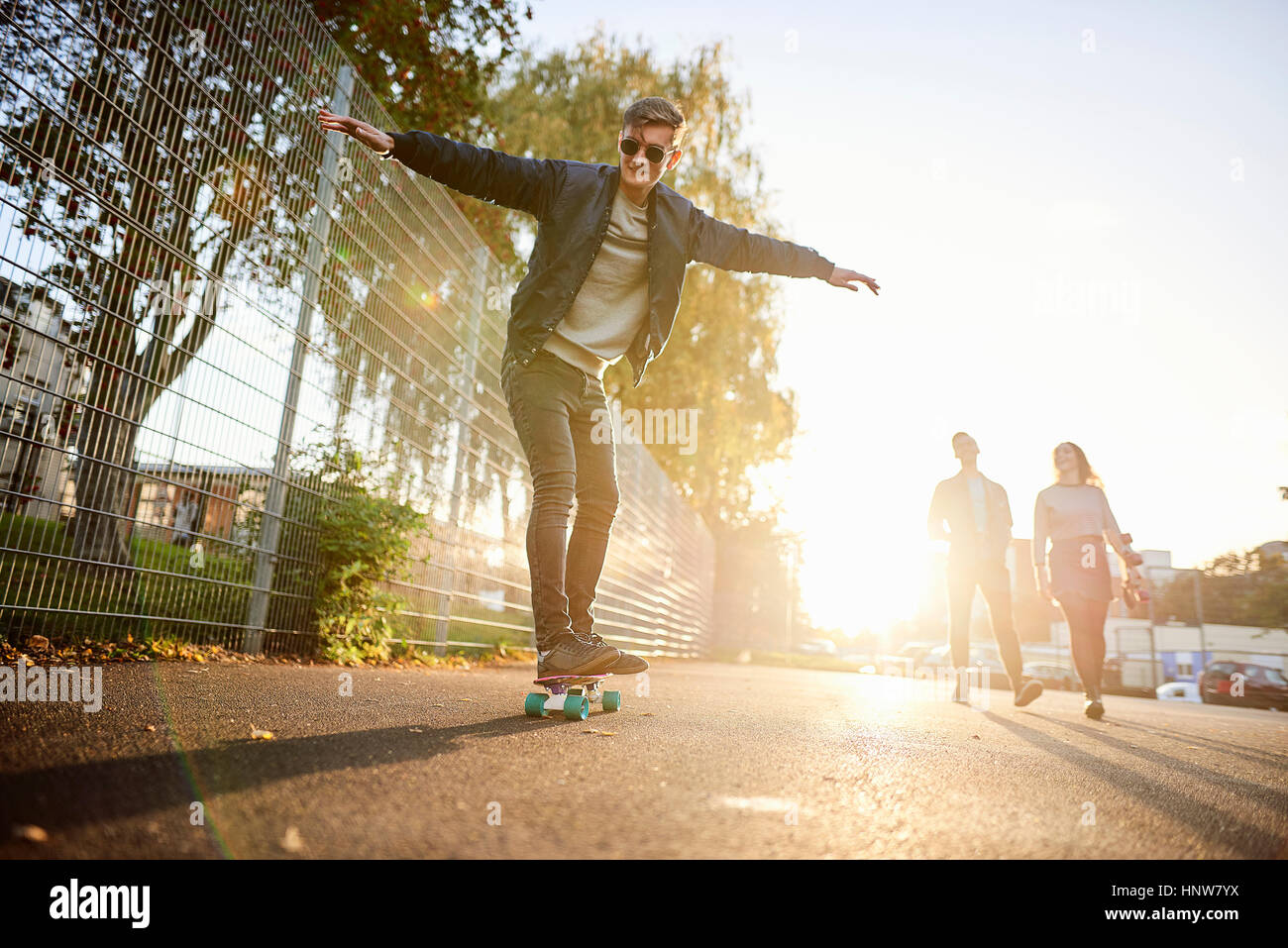 Junge männliche Skater Skateboard auf sonnendurchfluteten Straße Stockfoto