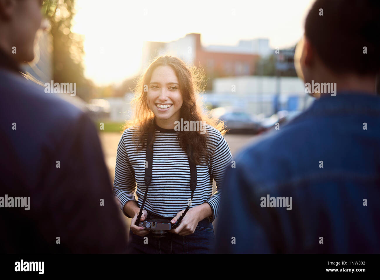 Über Schulter Blick der jungen Frau im Gespräch mit männlichen Freunden auf sonnendurchfluteten Straße Stockfoto