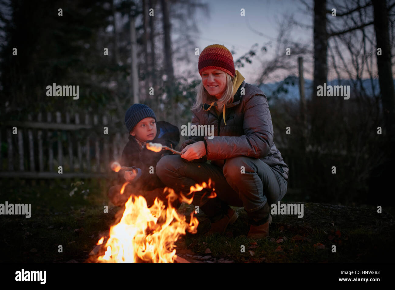 Reife Frau und Sohn Rösten Marshmallows auf Garten Lagerfeuer in der Dämmerung Stockfoto