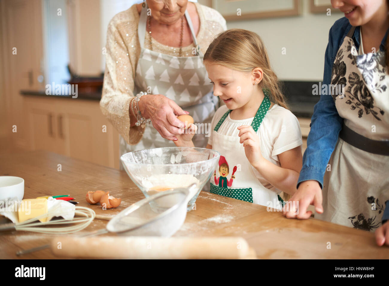 Ältere Frau und Enkelinnen knacken Eiern für cookies Stockfoto