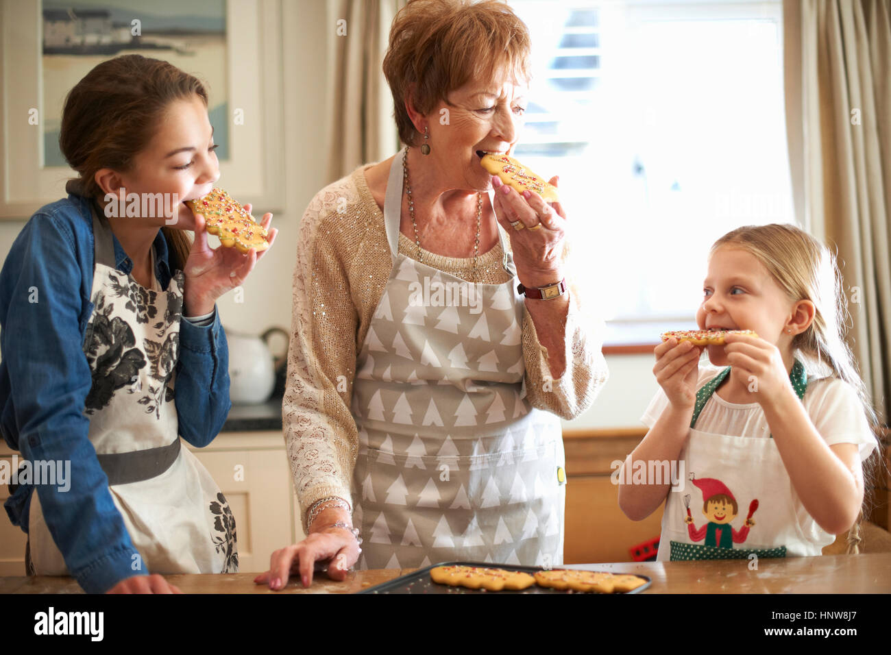 Ältere Frau und Enkelinnen Essen frisch gebackene Weihnachtsbaum Kekse Stockfoto