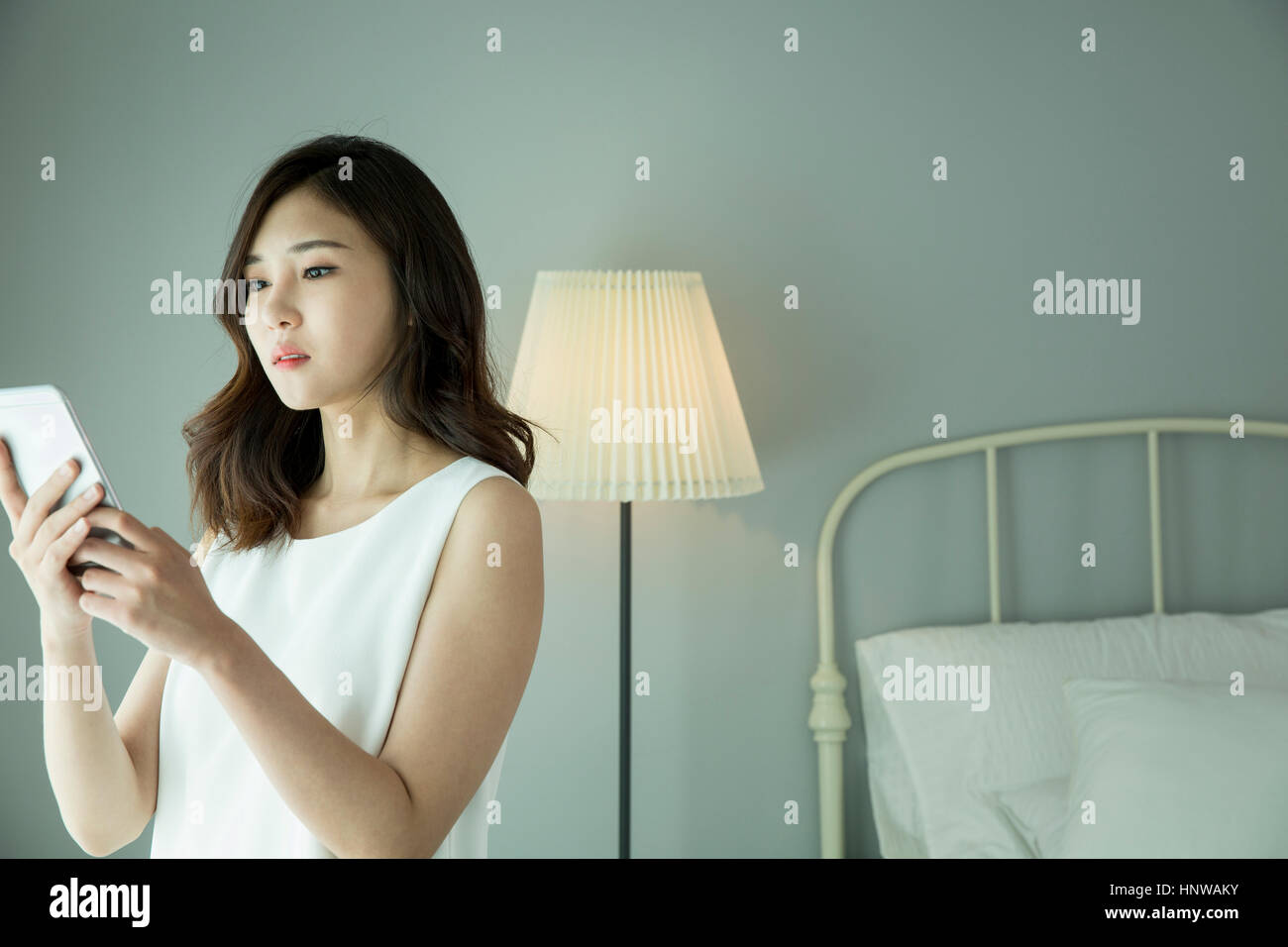 Junge Frau mit Smartphone im Schlafzimmer Stockfoto