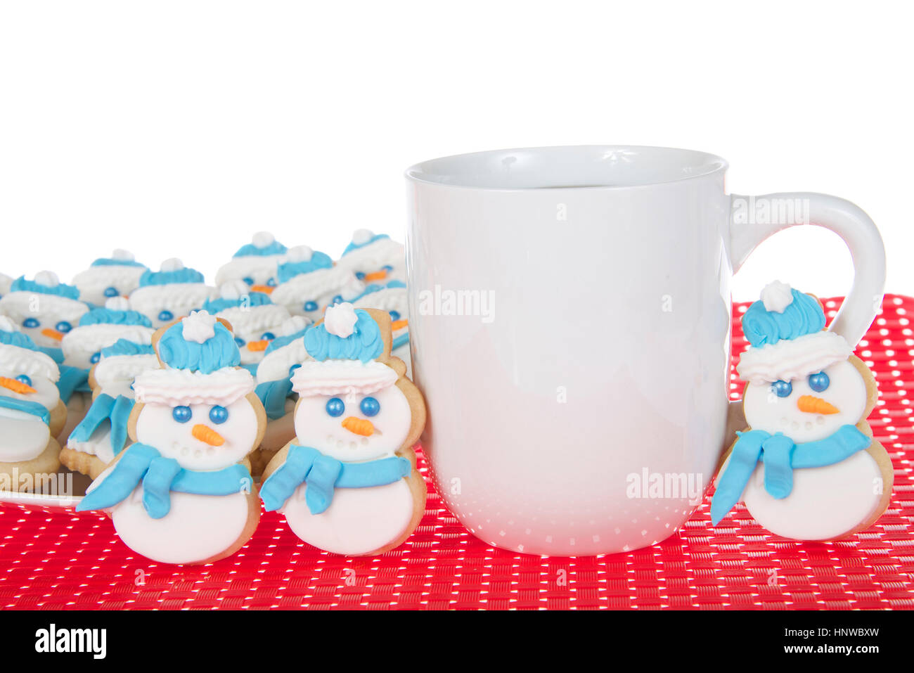 Schneemann-Butterkekse mit königlicher Zuckerglasur Zuckerguss Schals und Mützen sitzt auf einem weißen Teller auf roten Stoff Tischset mit Tasse Kaffee. Drei cookies Stockfoto