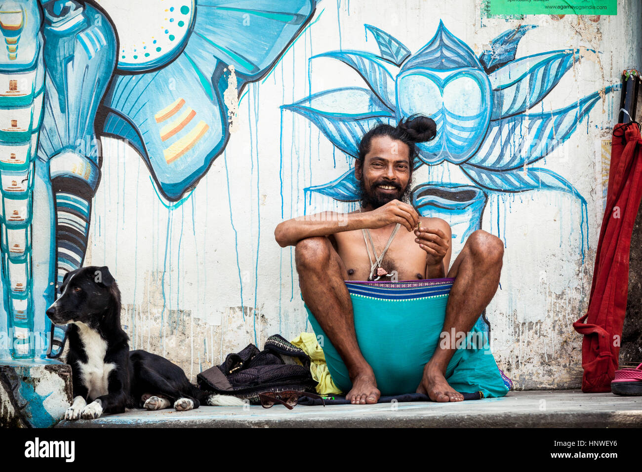 Rishikesh, Indien - 22. September 2014: Junge Pilger mit Hund sitzt in der Nähe der Wand gemalt mit Straßenkunst in Rishikesh, Indien. Stockfoto