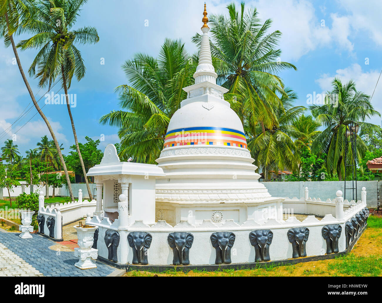 Die kleine weiße Stupa von Sri Devagiri Viharaya mit langen Turm und Zaun, verziert mit schwarzen Elefanten, Chilaw, Sri Lanka. Stockfoto