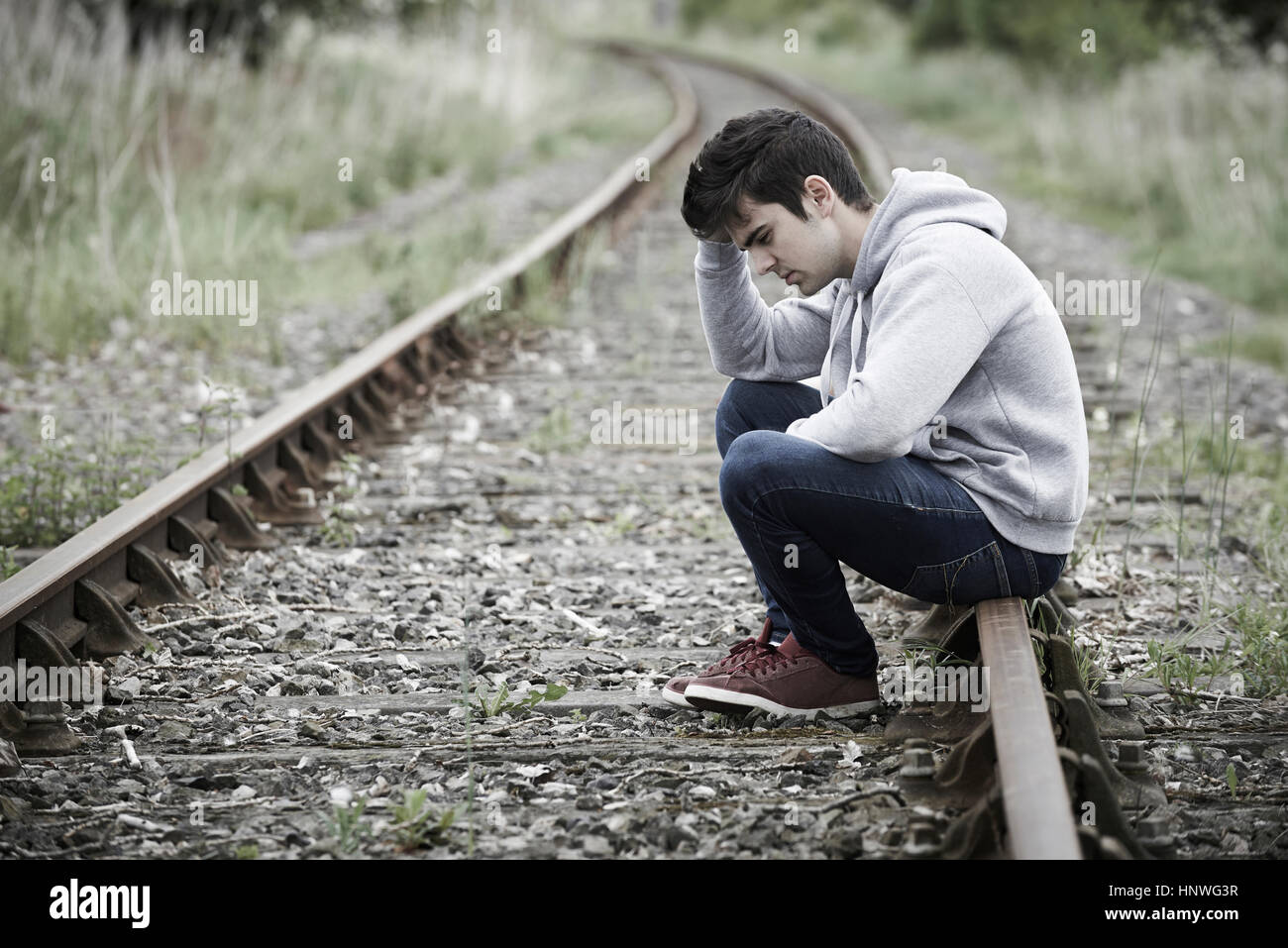 Deprimiert junger Mann sitzt auf Gleis Stockfoto