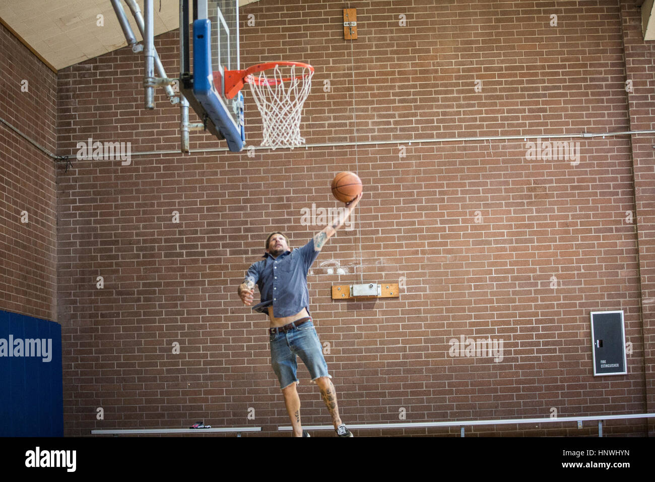 Tätowierte Mann springen und mit dem Ziel Ball in Richtung Basketballkorb auf Platz Stockfoto