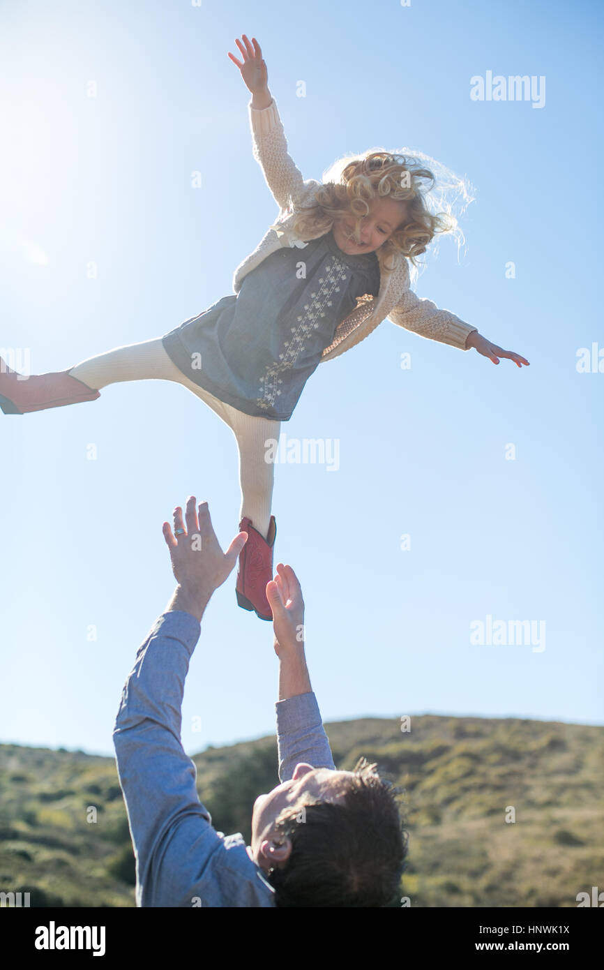 Mädchen, Luft von Vater gegen sonnigen blauen Himmel geworfen Stockfoto